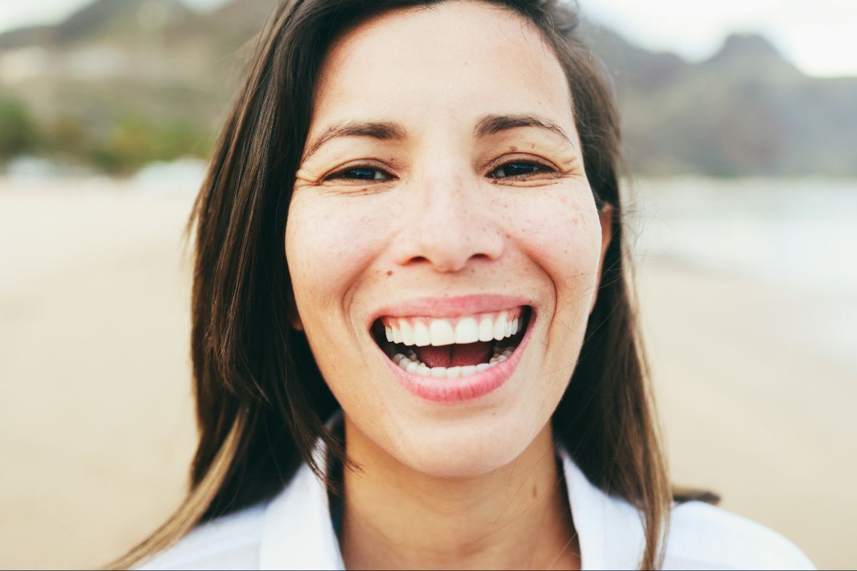 Woman with a bright, healthy smile outdoors at a beach location.