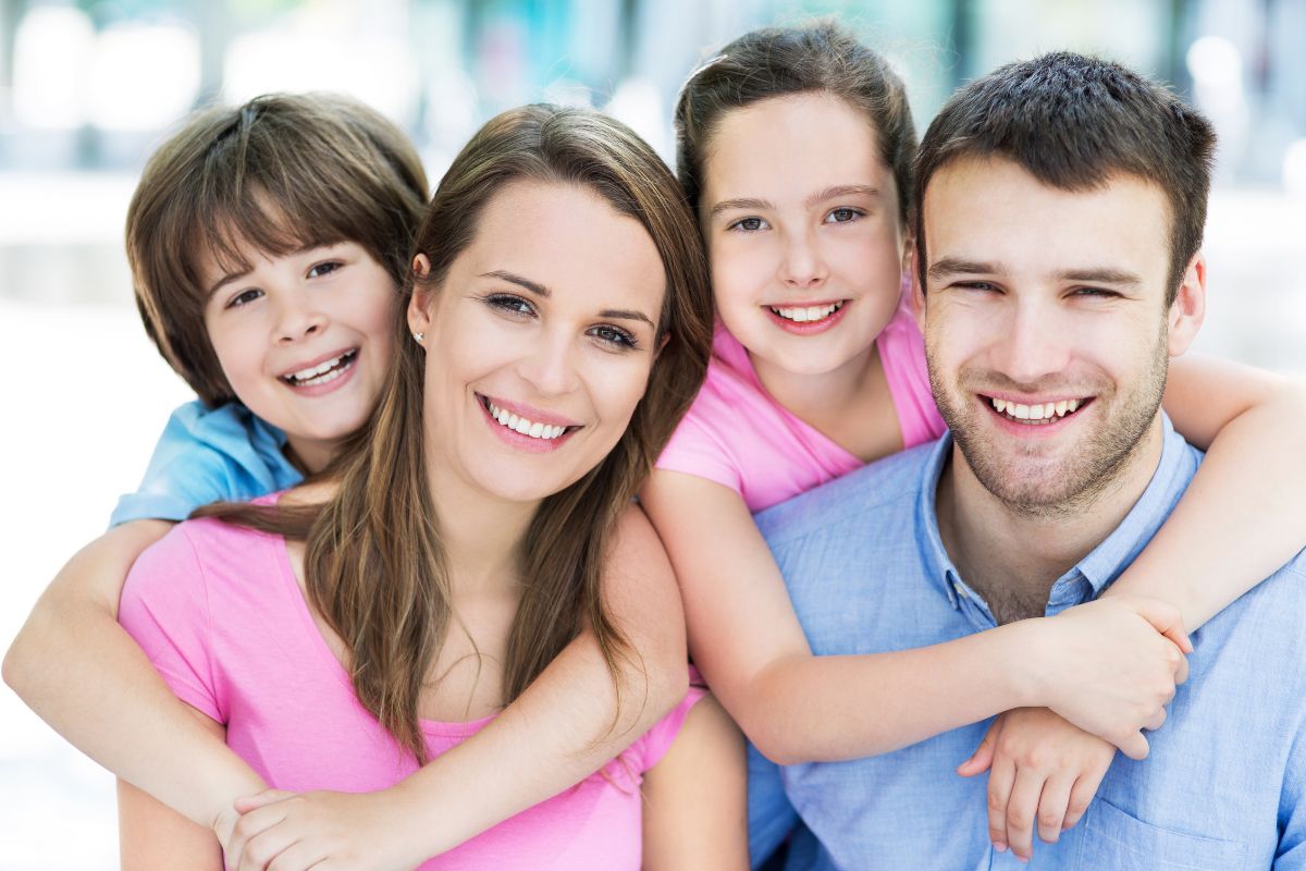 Happy family of four smiling together in casual colorful clothing indoors.