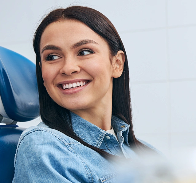 Smiling woman in denim shirt at dental office, looking back at camera in professional setting.